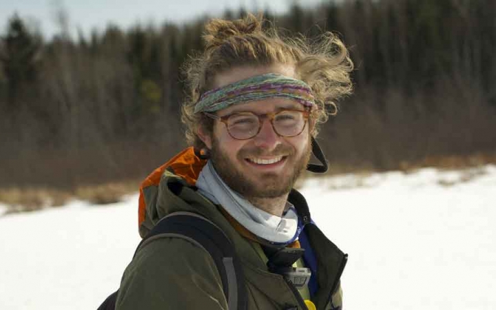a gap year student smiles at the camera while standing in a field of snow. there are trees in the background.